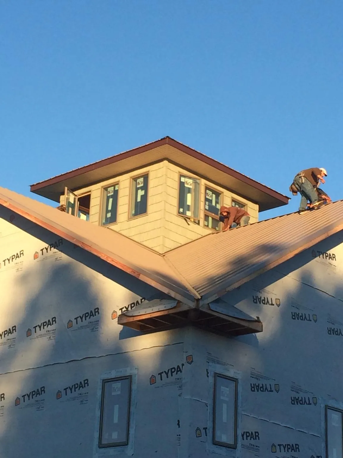 Roofers working around a rooftop cupola on a new metal roof at sunset in Richmond
